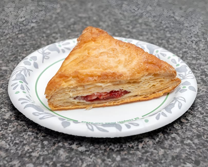 A triangular guava and cheese pastry on a white paper plate with a green and gray floral design.